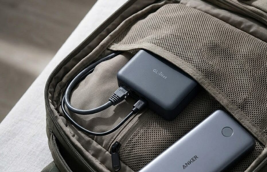 A small black GL.iNet Opal travel router tucked into the tech compartment of a travel backpack with cables organized.